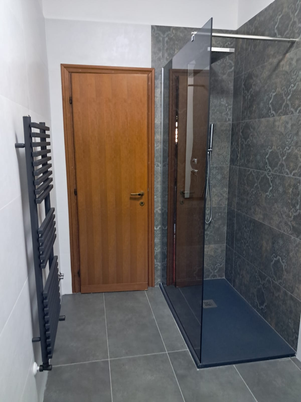Doccia walk-in su piastrelle scure e porta in legno
